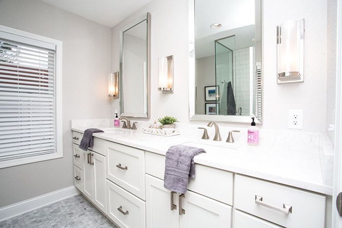 A bathroom with two sinks , two mirrors , and a window.