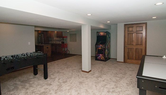 A basement with a pool table , foosball table , and arcade machine.
