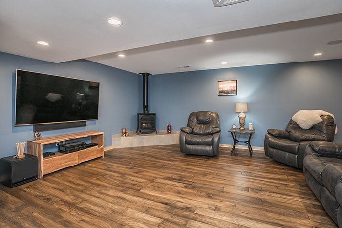 A living room with hardwood floors , two chairs , a flat screen tv and a fireplace.