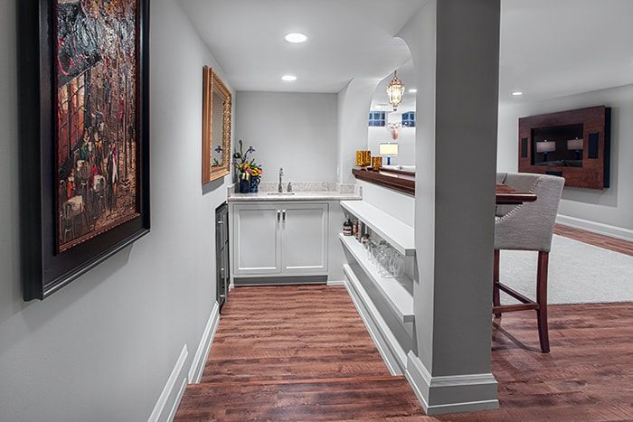 A hallway in a basement with hardwood floors and a sink.