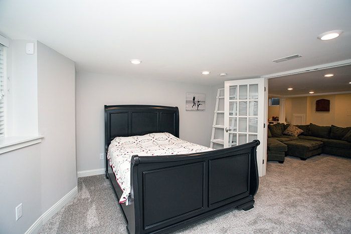 A bedroom in a basement with a bed and a couch.