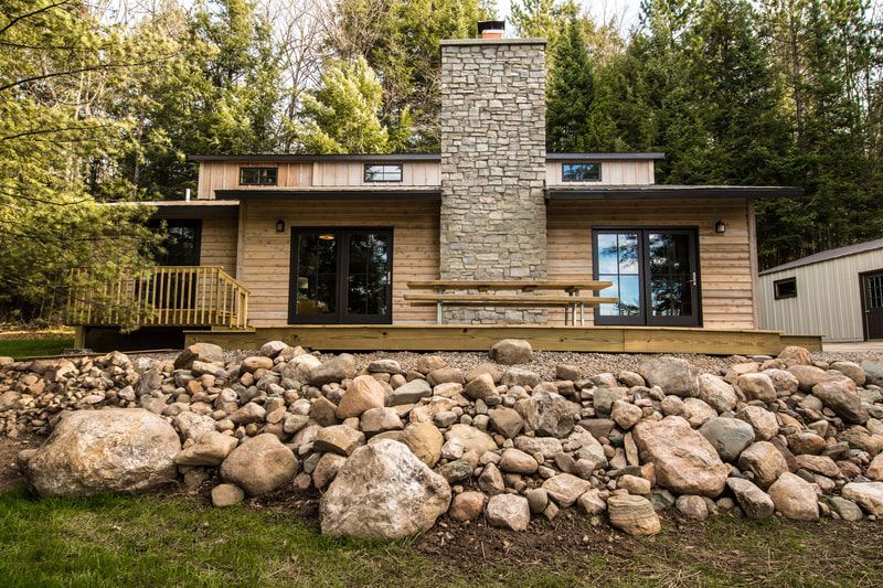 A house with a stone chimney and a large rock wall in front of it.
