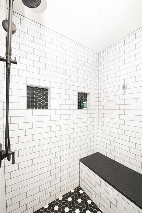 A shower with white brick walls and a black bench.