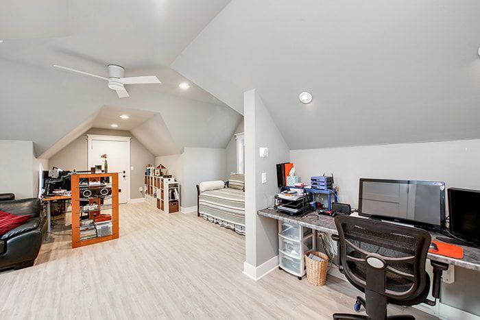 A room with a desk , chair , computer and a ceiling fan.