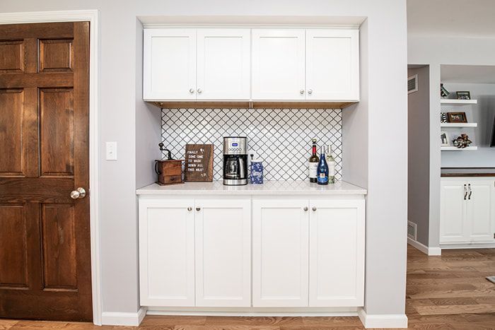 A kitchen with white cabinets , a coffee maker , and a bar.
