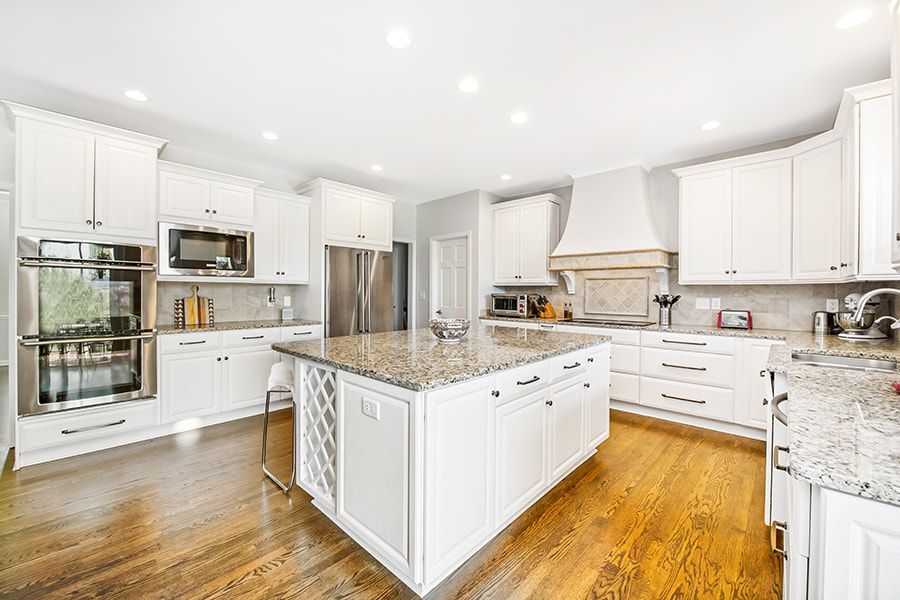A kitchen with white cabinets , granite counter tops , stainless steel appliances and hardwood floors.