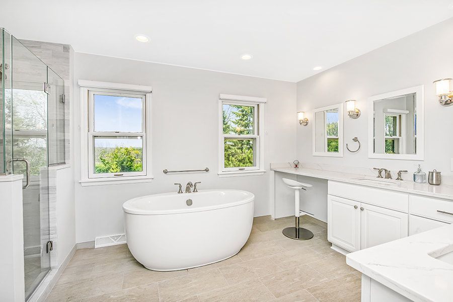 A bathroom with a tub , sink , mirror and window.