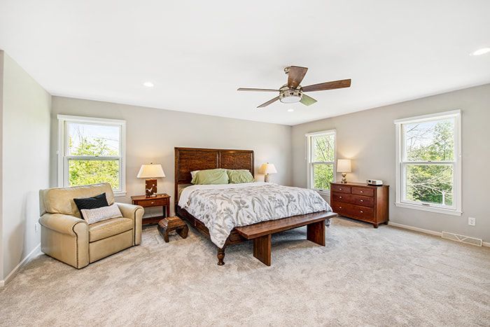 A bedroom with a bed , chair , dresser , and ceiling fan.