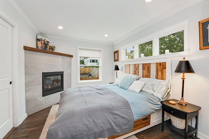 A bedroom with a bed , nightstand , lamp and fireplace.