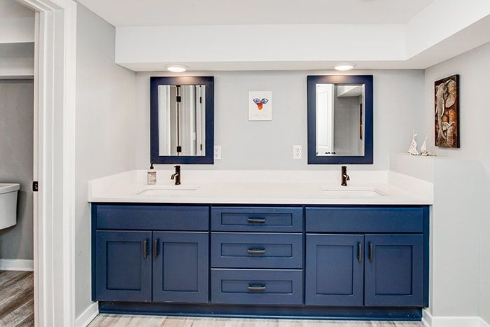 A bathroom with two sinks , two mirrors and blue cabinets.