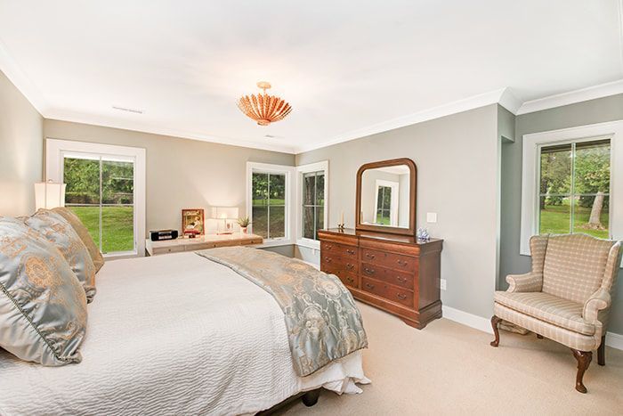A bedroom with a large bed , dresser , chair and mirror.