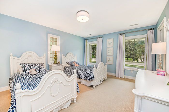 A bedroom with two beds , a dresser , and two windows.