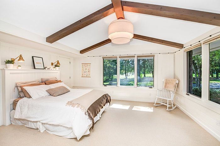A bedroom with a bed , rocking chair , and lots of windows.