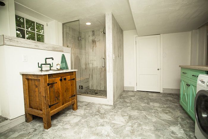 A bathroom with a sink , washer and dryer , and a walk in shower.