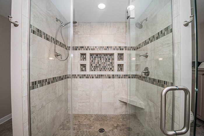 A walk in shower with a glass door and a bench.