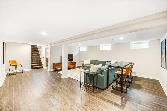A living room in a basement with a couch , table and chairs.