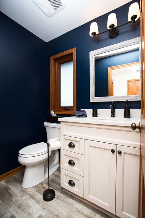 A bathroom with a toilet , sink , mirror and blue walls.