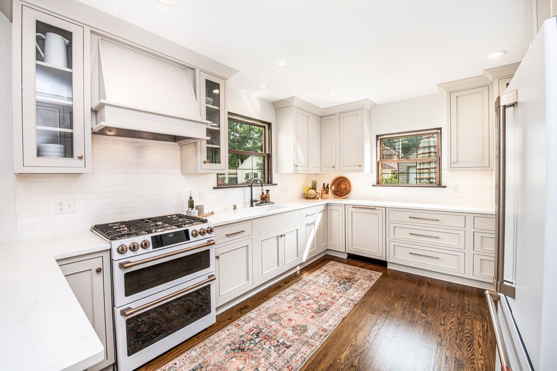 A kitchen with white cabinets , a stove , a refrigerator , and a rug.