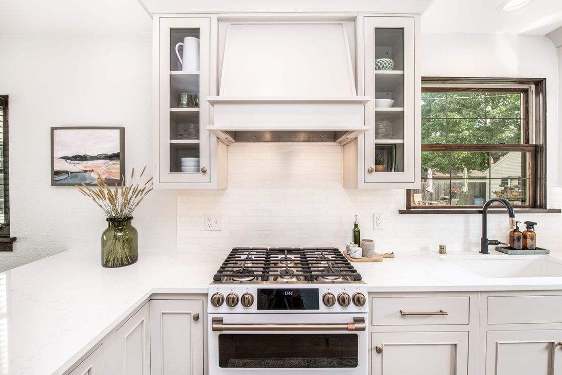 A kitchen with white cabinets , a stove , a sink , and a window.