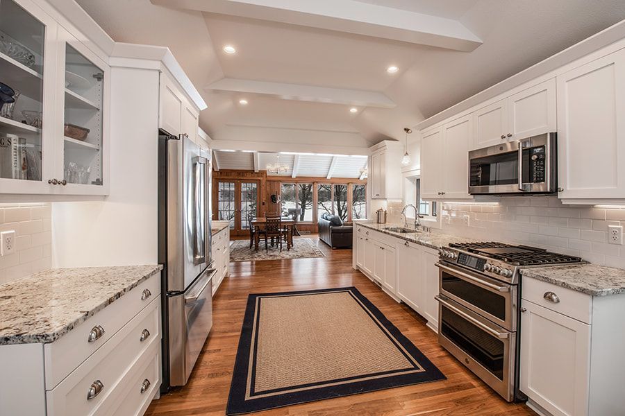 A kitchen with white cabinets , granite counter tops , stainless steel appliances and a rug.