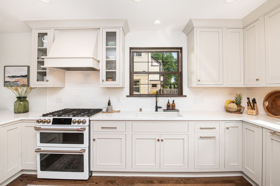 A kitchen with white cabinets , a stove , a sink , and a window.