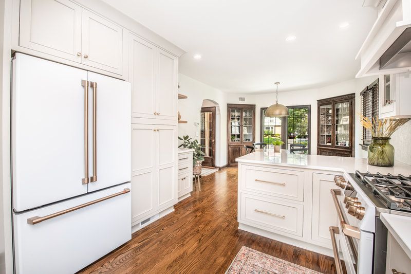 A kitchen with white cabinets , a white refrigerator , a stove , and a large island.