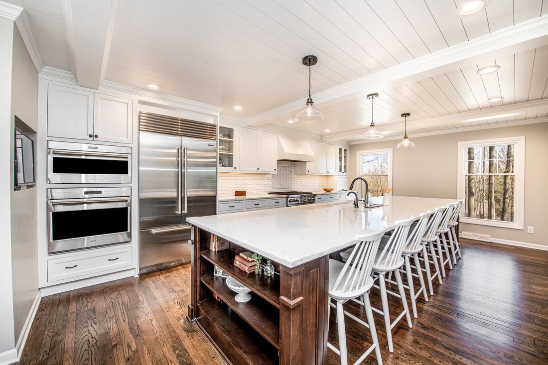 A kitchen with white cabinets , stainless steel appliances , a large island , and hardwood floors.