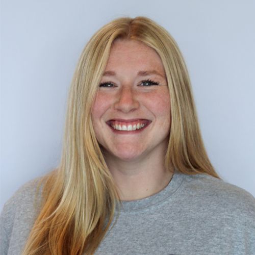 A woman with long blonde hair is smiling and wearing a grey shirt.