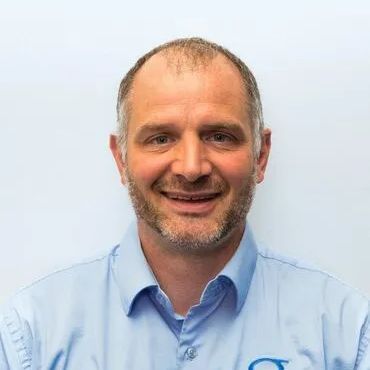A man with a beard is wearing a blue shirt and smiling.