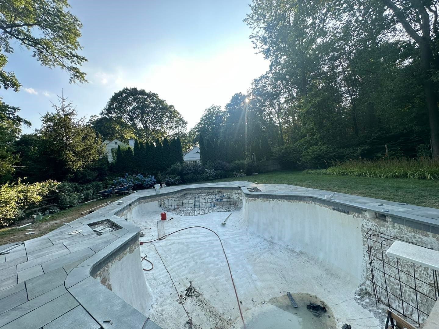 An empty swimming pool in a backyard with trees in the background.