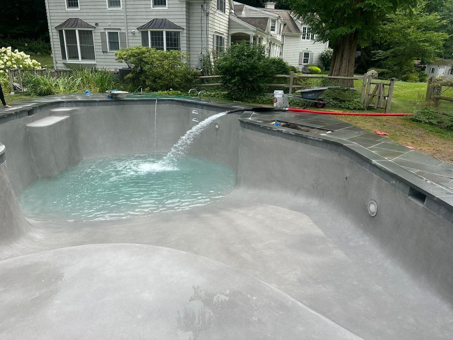 A swimming pool with a fountain in the middle of it in front of a house.