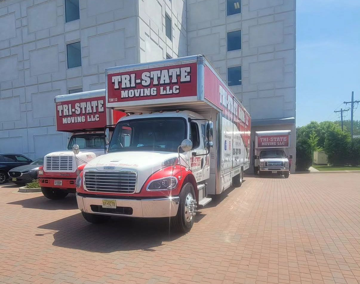 Two Tri-State Moving LLC trucks parked on a brick lot beside a building.