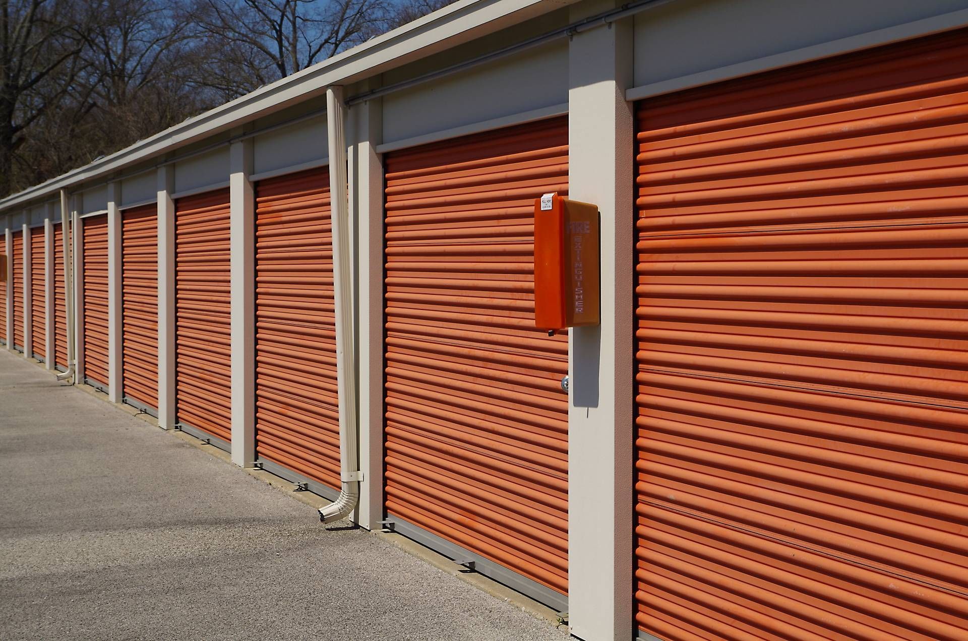 Row of orange storage unit doors along a paved outdoor facility under a blue sky