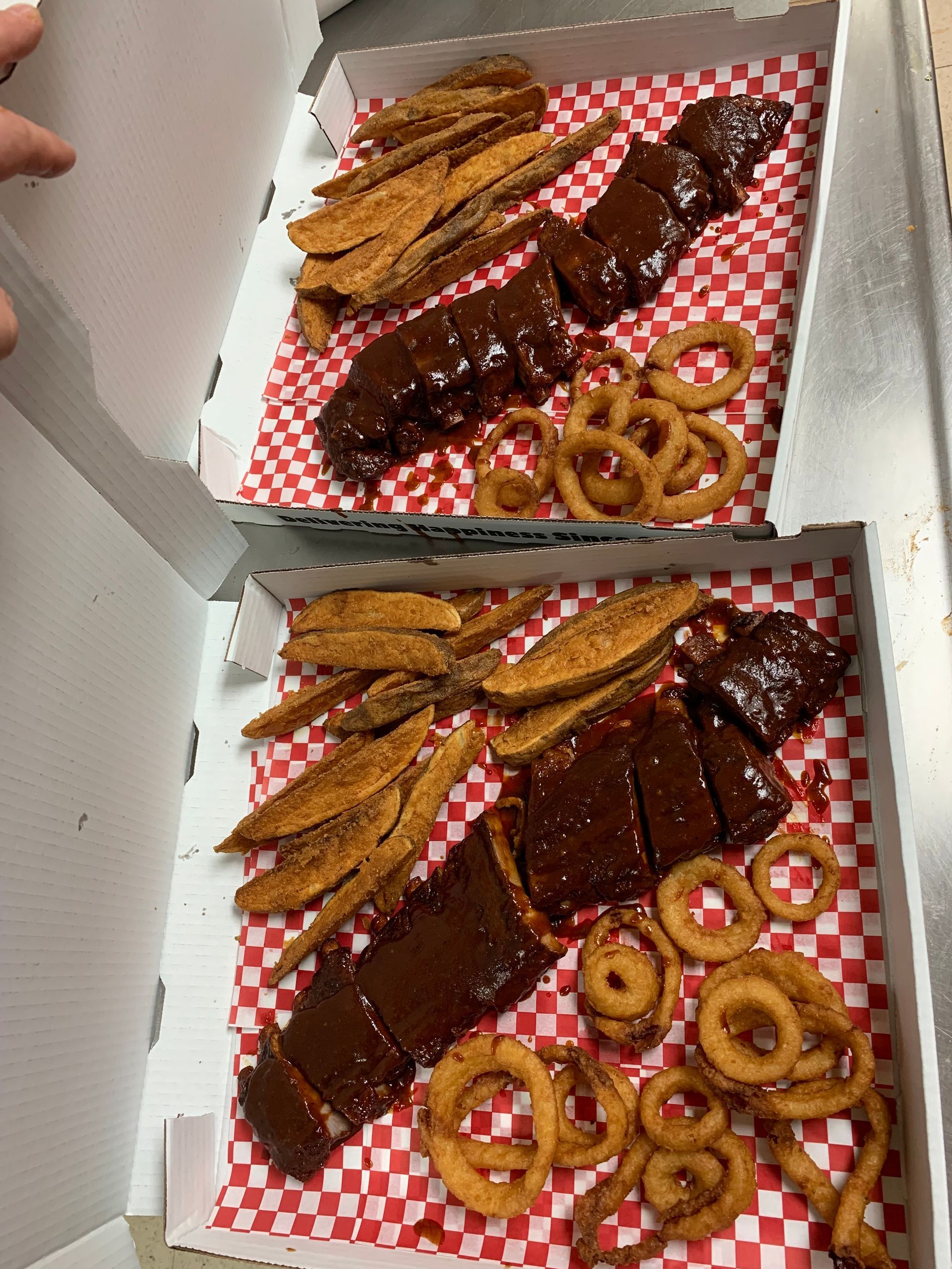 Two pizza boxes filled with ribs , fries , and onion rings.