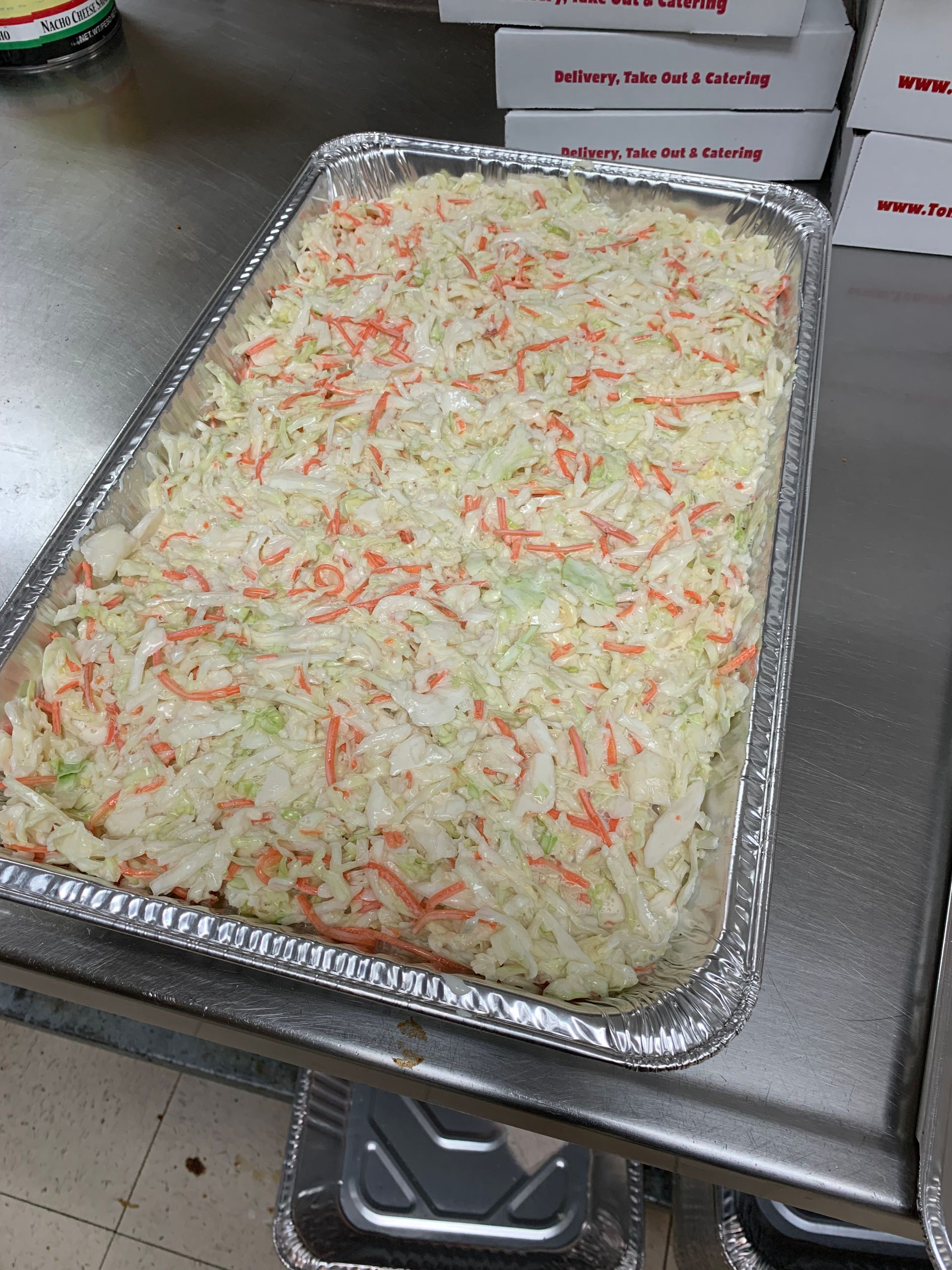 A large tray of coleslaw is sitting on a counter.