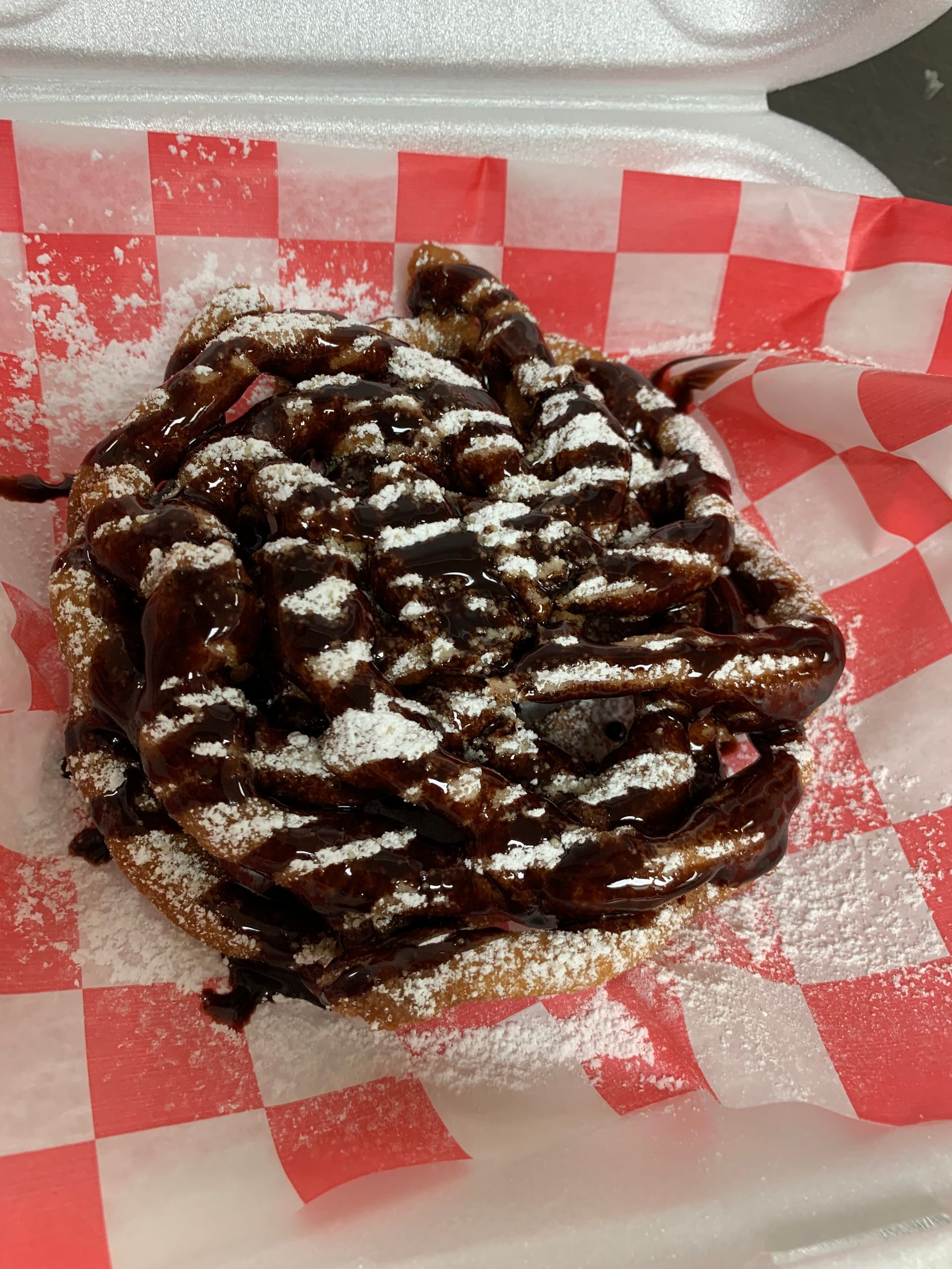 A close up of a waffle with chocolate sauce and powdered sugar in a styrofoam container.