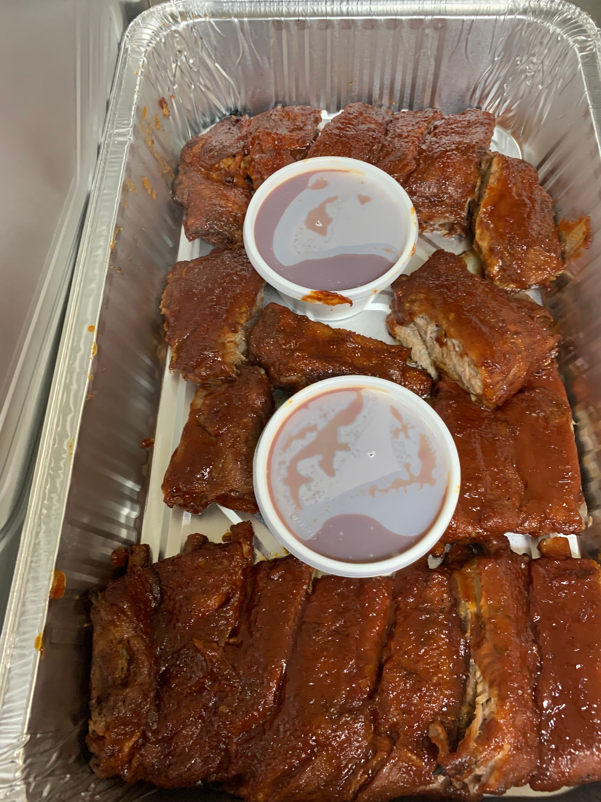 A tray of ribs with two dipping sauces on top.