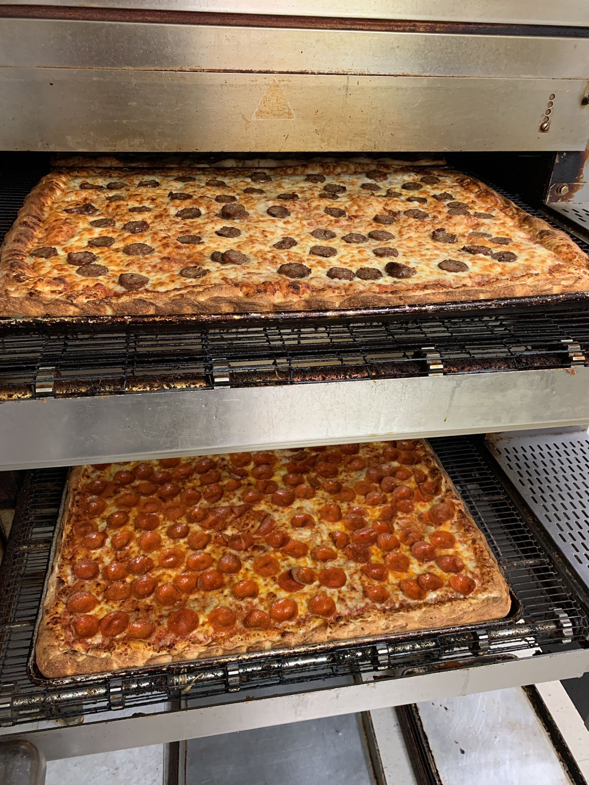Two pepperoni pizzas are sitting on a rack in an oven.