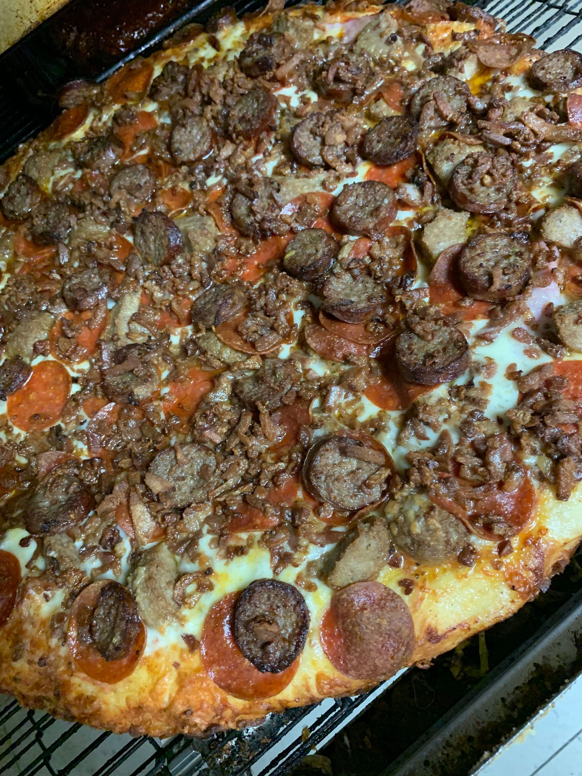 A pizza with pepperoni , sausage , mushrooms and cheese is sitting on a cooling rack.