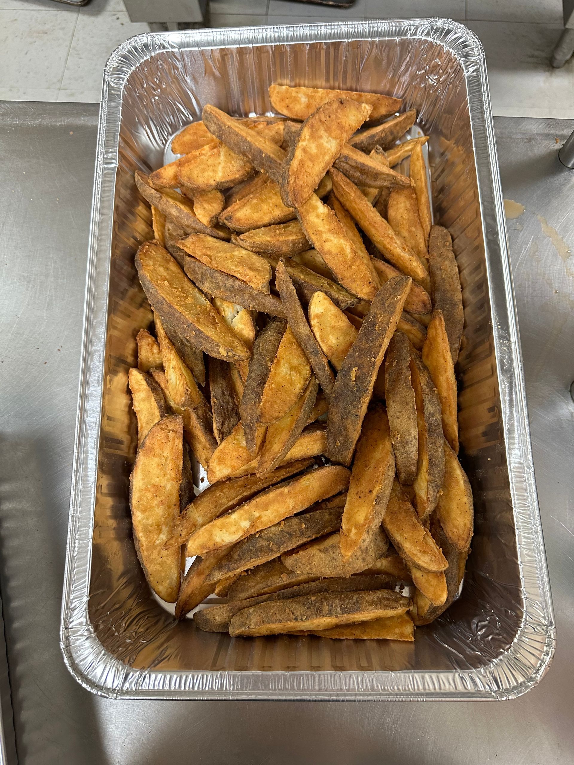 A tin foil container filled with french fries on a counter.