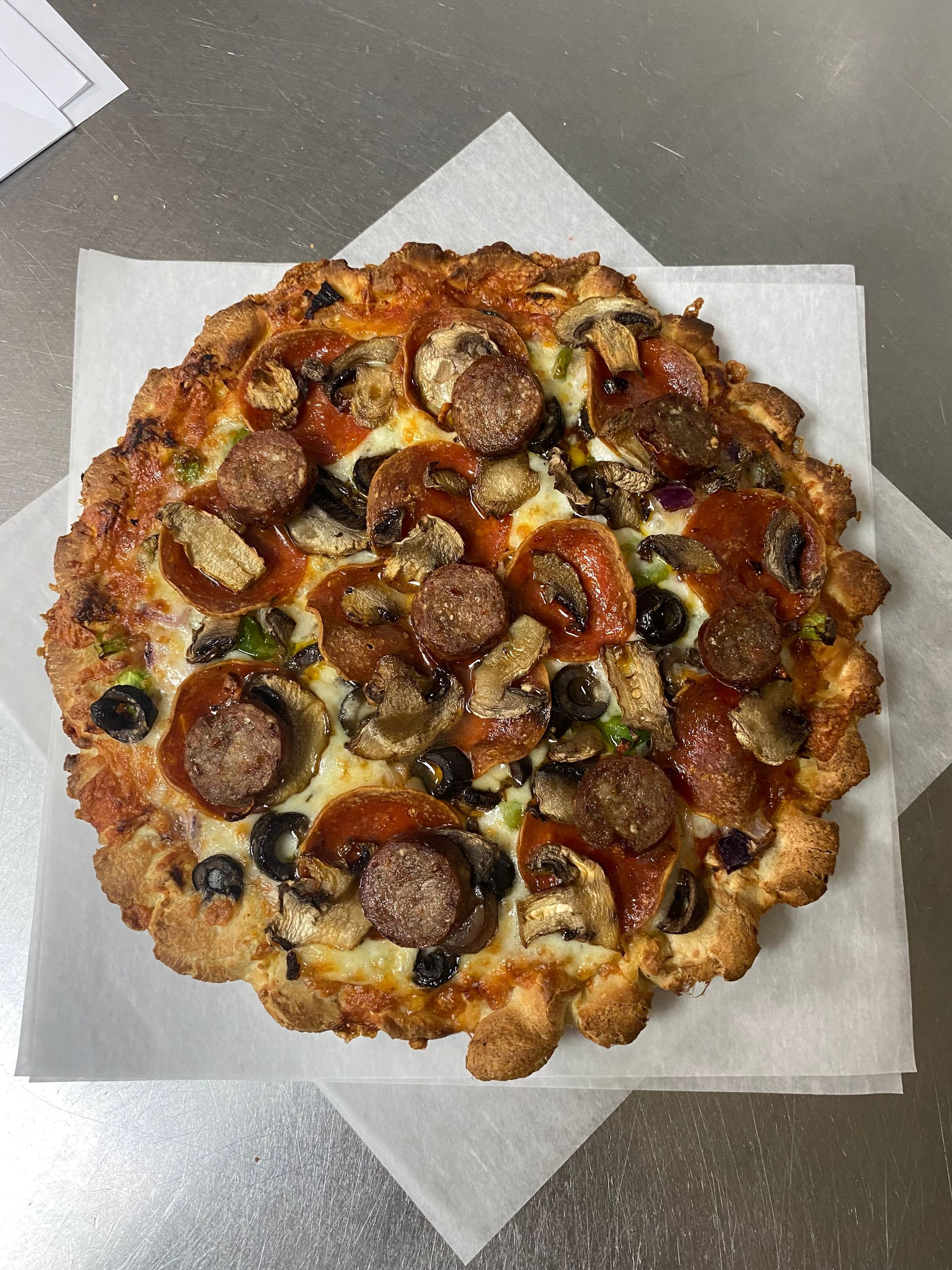 A pizza with pepperoni mushrooms olives and cheese on a piece of wax paper