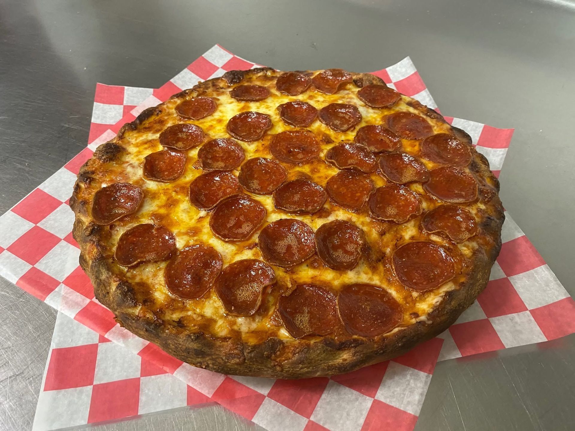 A pepperoni pizza is sitting on a checkered napkin on a table.