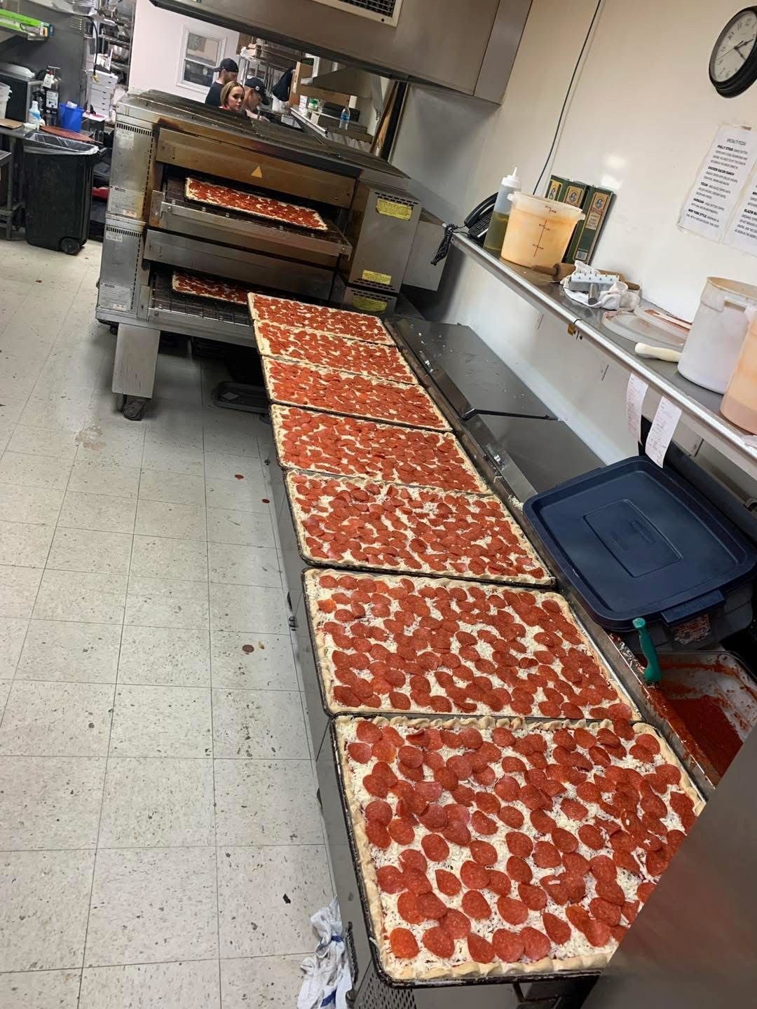 A row of pepperoni pizzas are sitting on a conveyor belt in a kitchen.