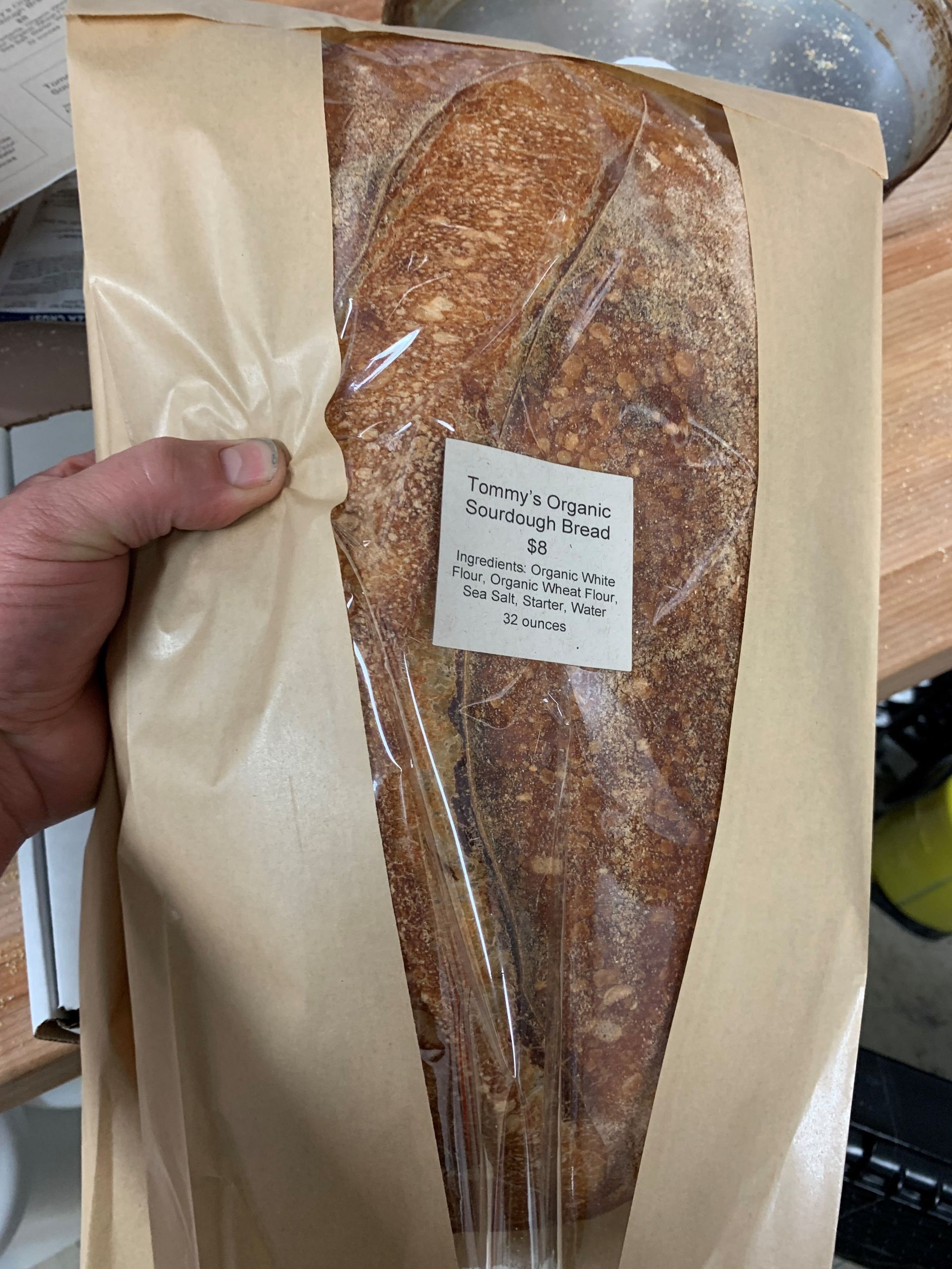 A person is holding a loaf of bread wrapped in brown paper.