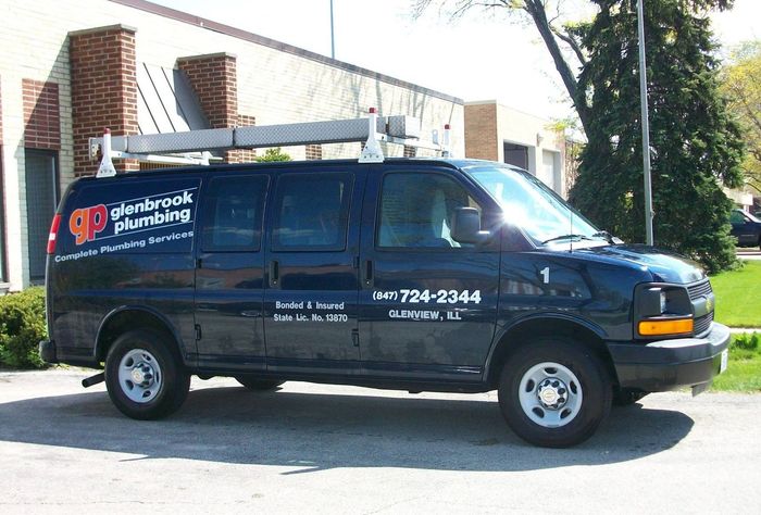 A plumbing van is parked in front of a building.