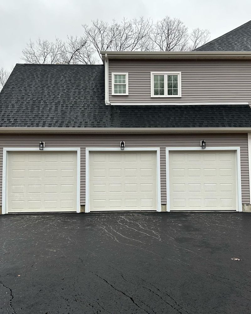 Three-car garage with white doors, gray siding, and a dark roof. Asphalt driveway.