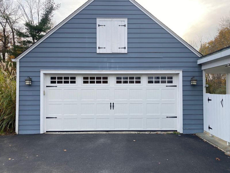 White garage door with black hardware on a blue-sided building with two sconces.