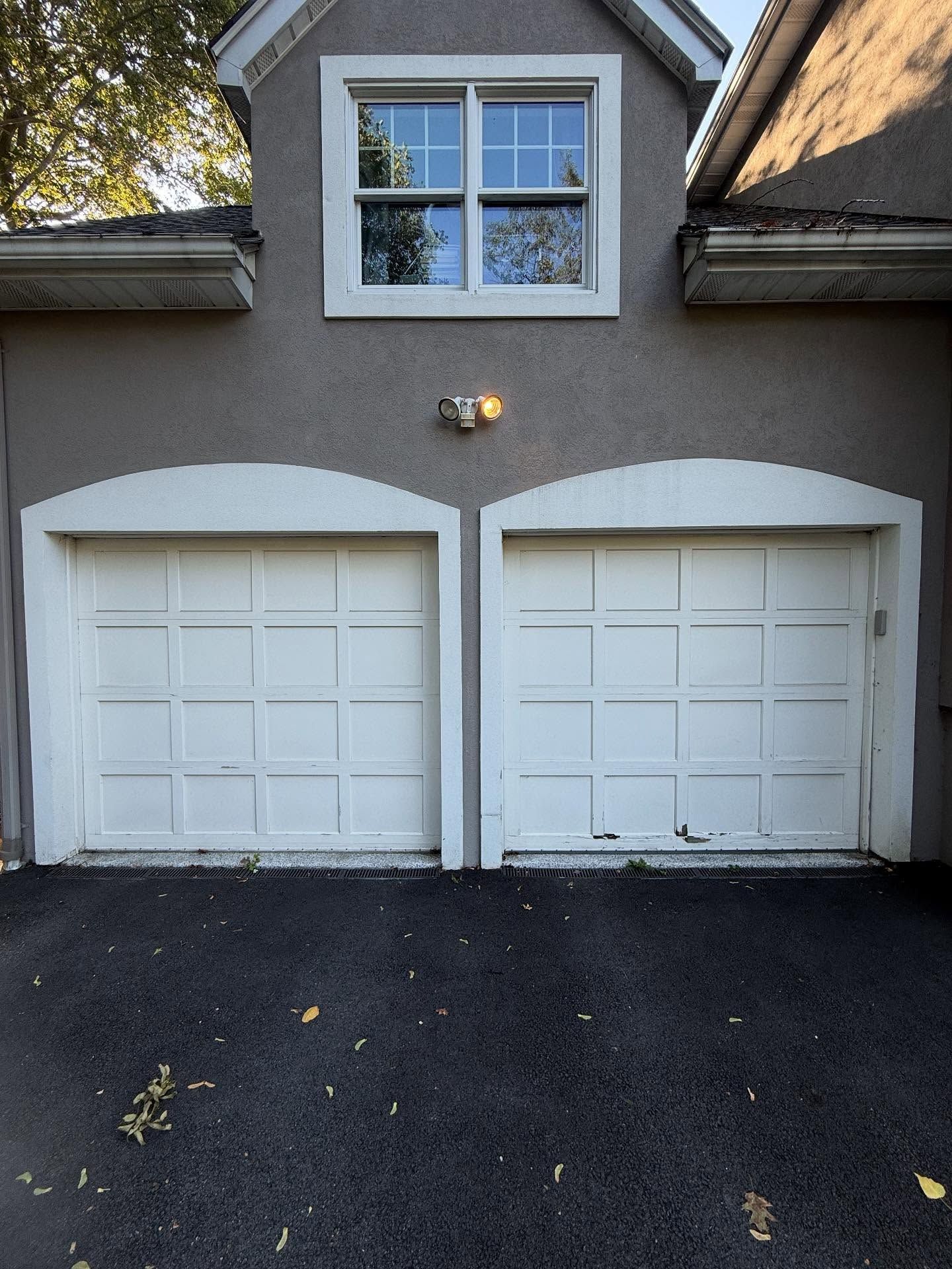 Two white garage doors with a window above, set in a stucco building.