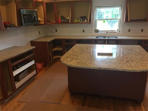 Kitchen undergoing renovation with brown cabinets and granite countertops. Island in foreground.