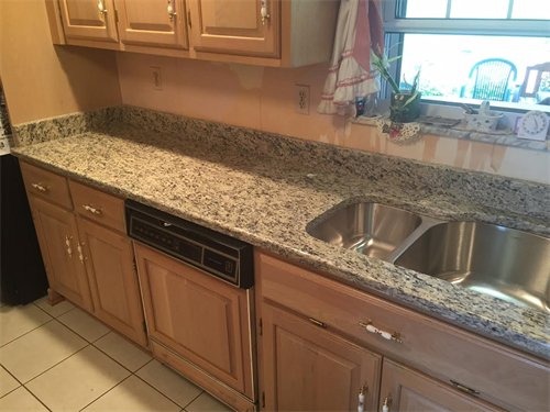 Kitchen with light wood cabinets, granite countertop, stainless steel sink, and a window.